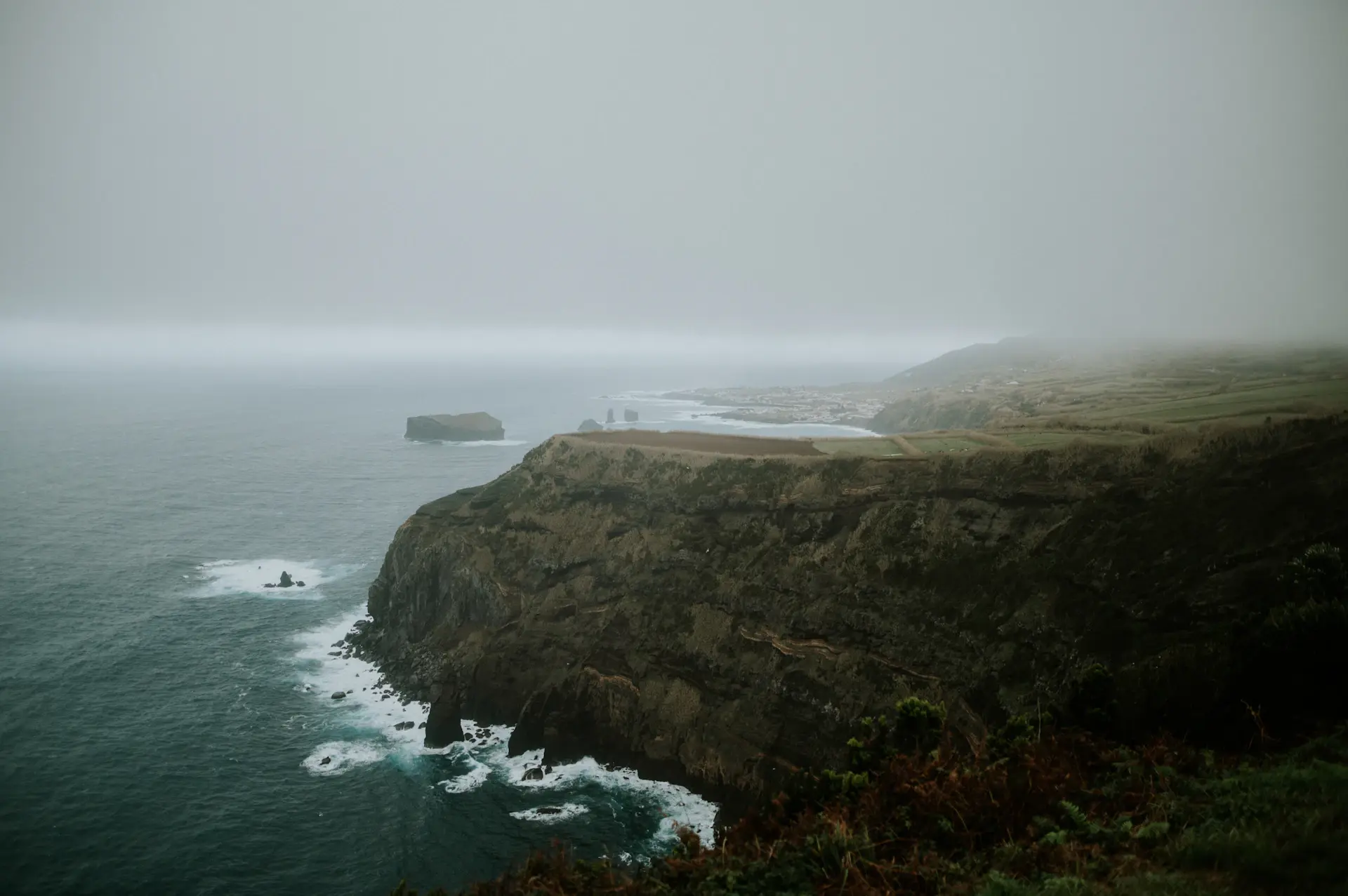 Lone mist-wrapped island cliff rising from a still grey sea at first light