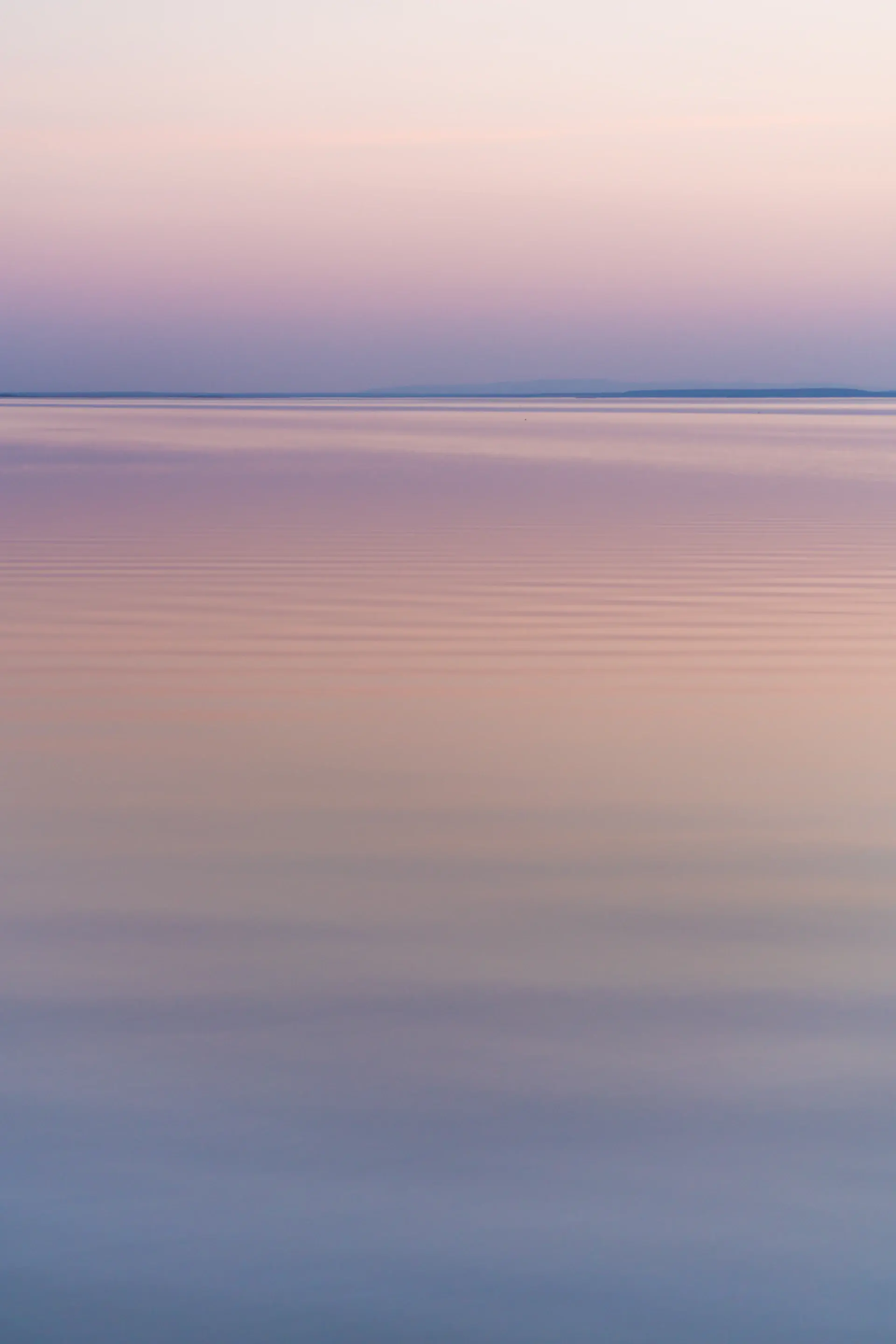 Mirror-calm sea at dawn with soft pastel light