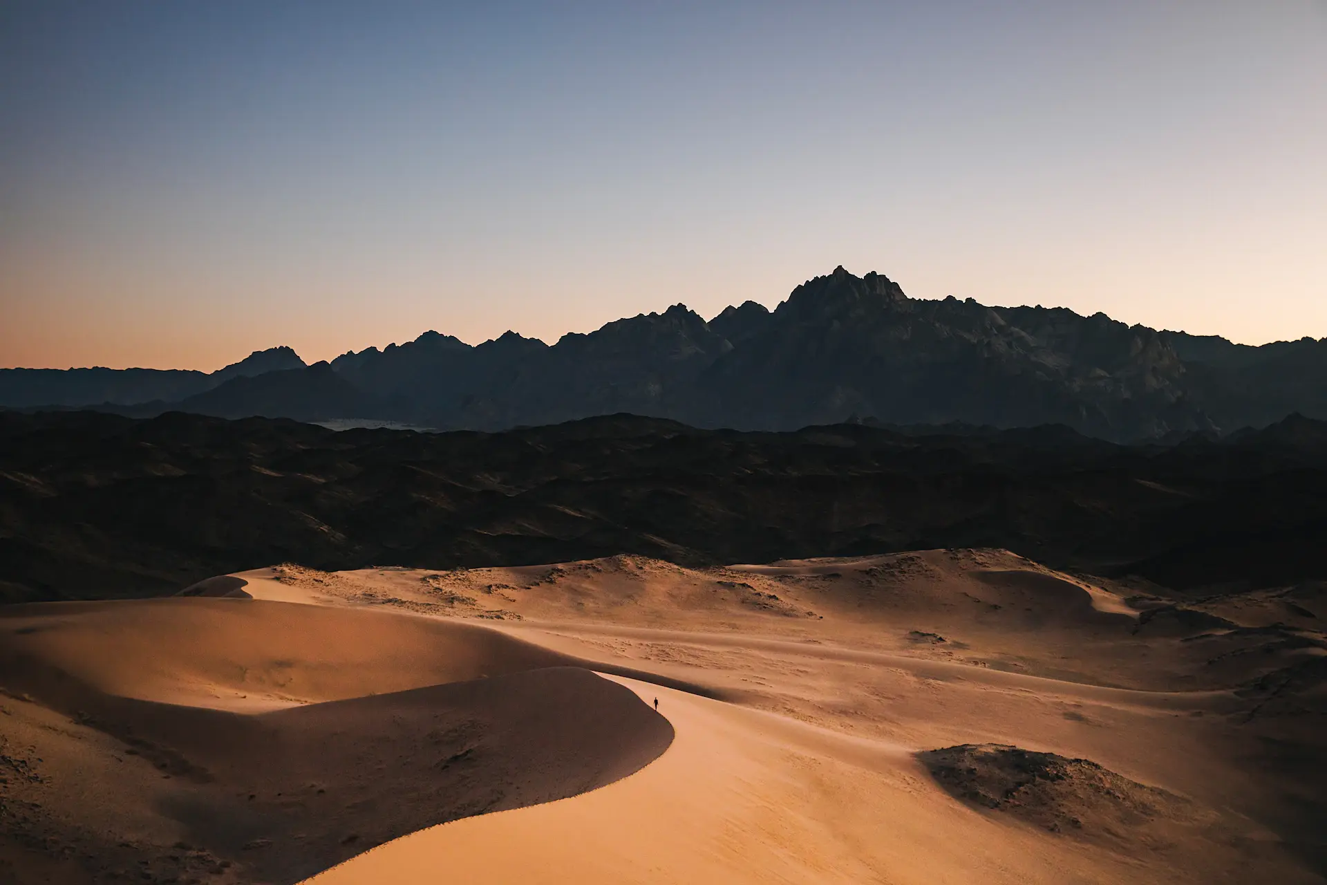 A solitary luxury camp beneath vast desert dunes at dusk