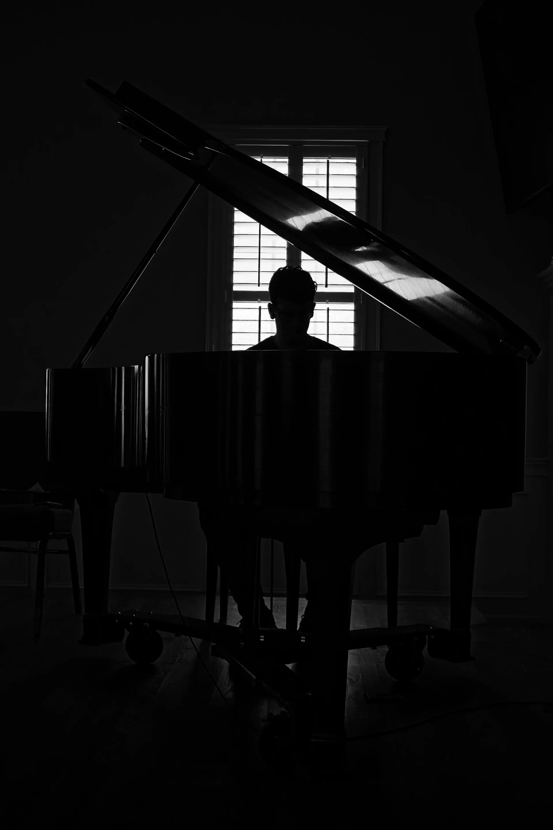 Silhouette nam giới đeo kính, ngồi bên chiếc dương cầm