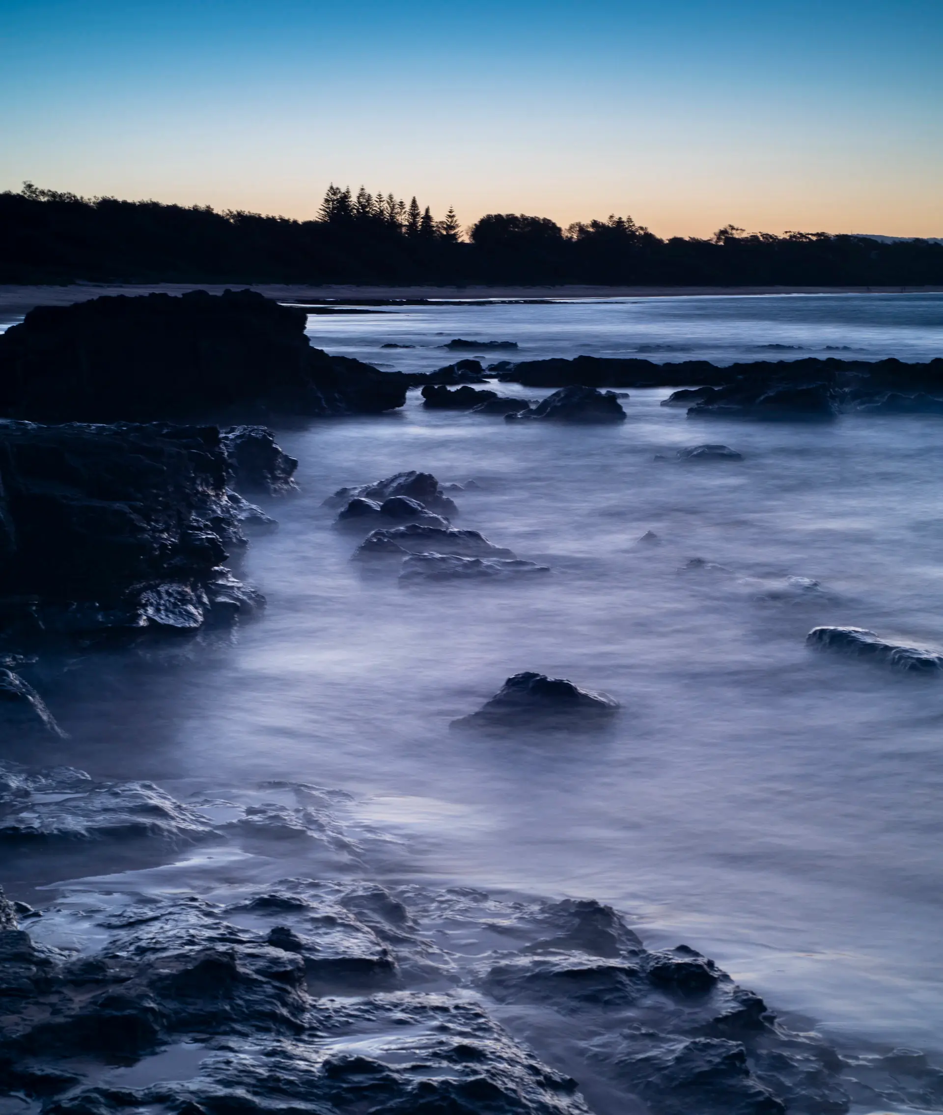 Long-exposure waves washing over dark coastal rocks at dusk
