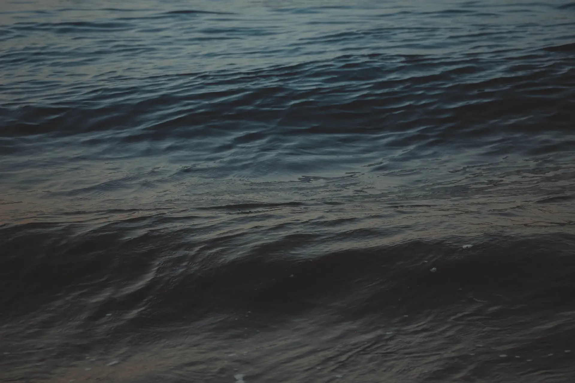 Dark cinematic ocean swell breaking under a pale northern sky