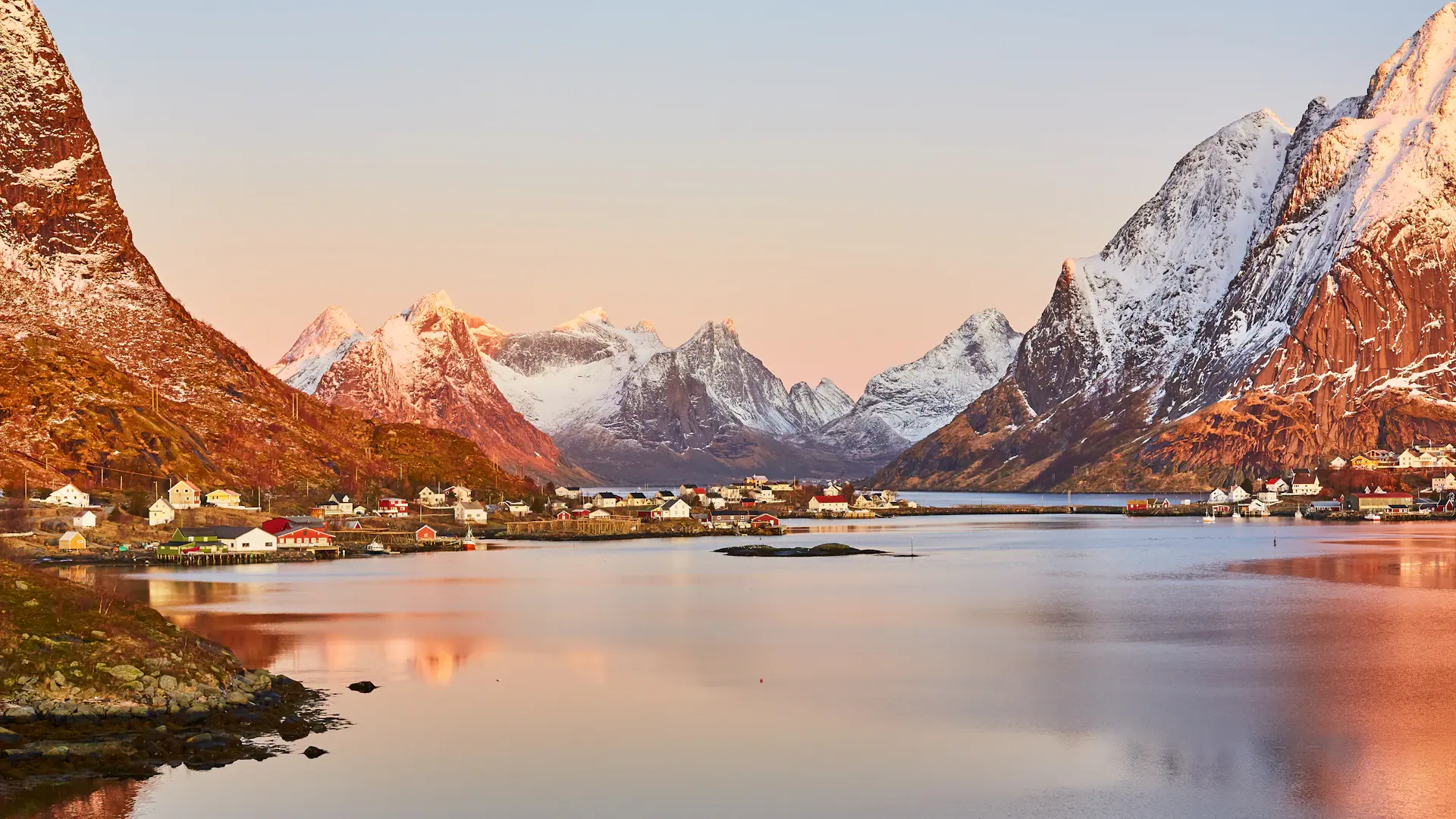 Glassy fjord mirroring snow peaks under a wide pastel evening sky