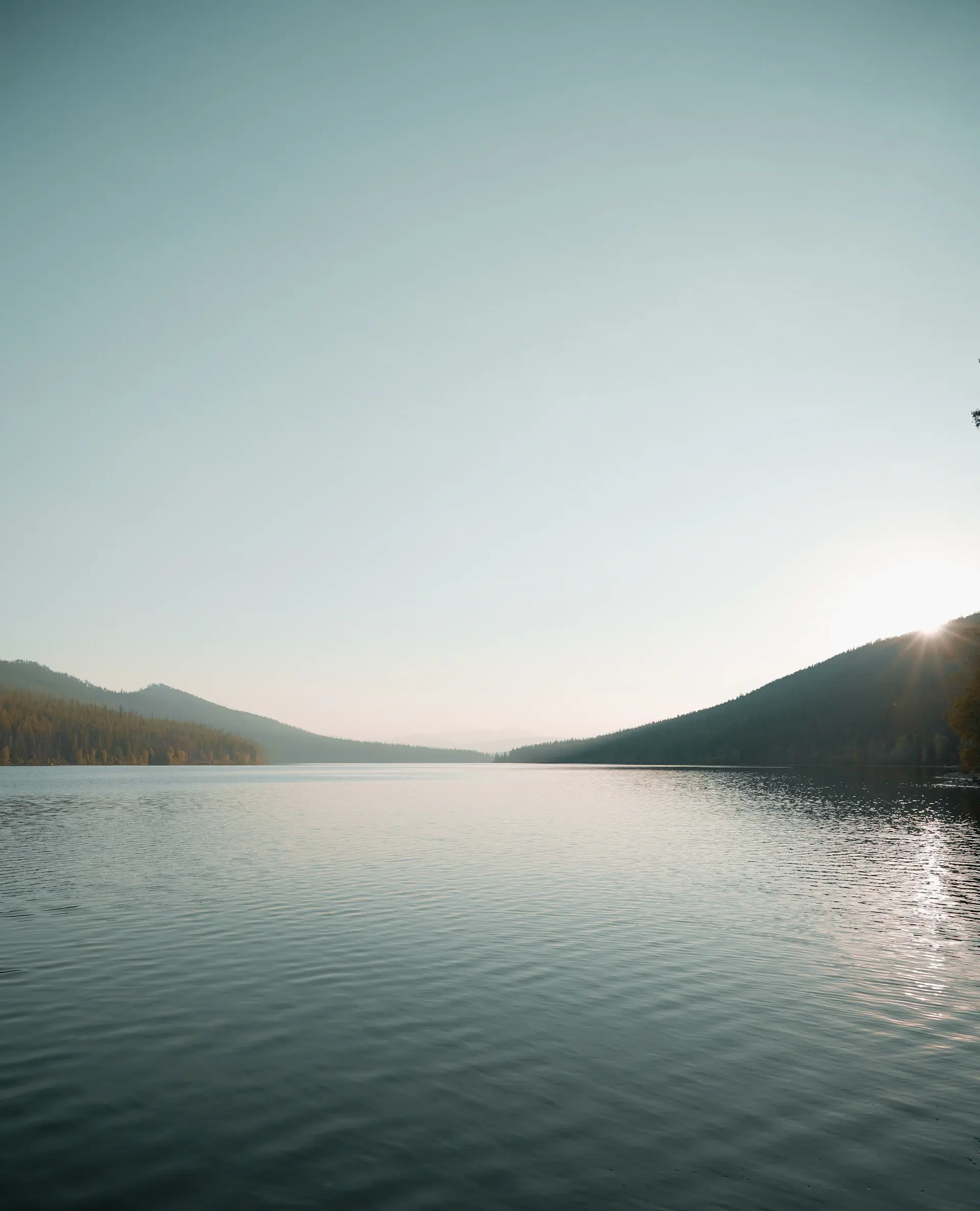 Mirror-still lake reflecting peaks under a pale morning sky