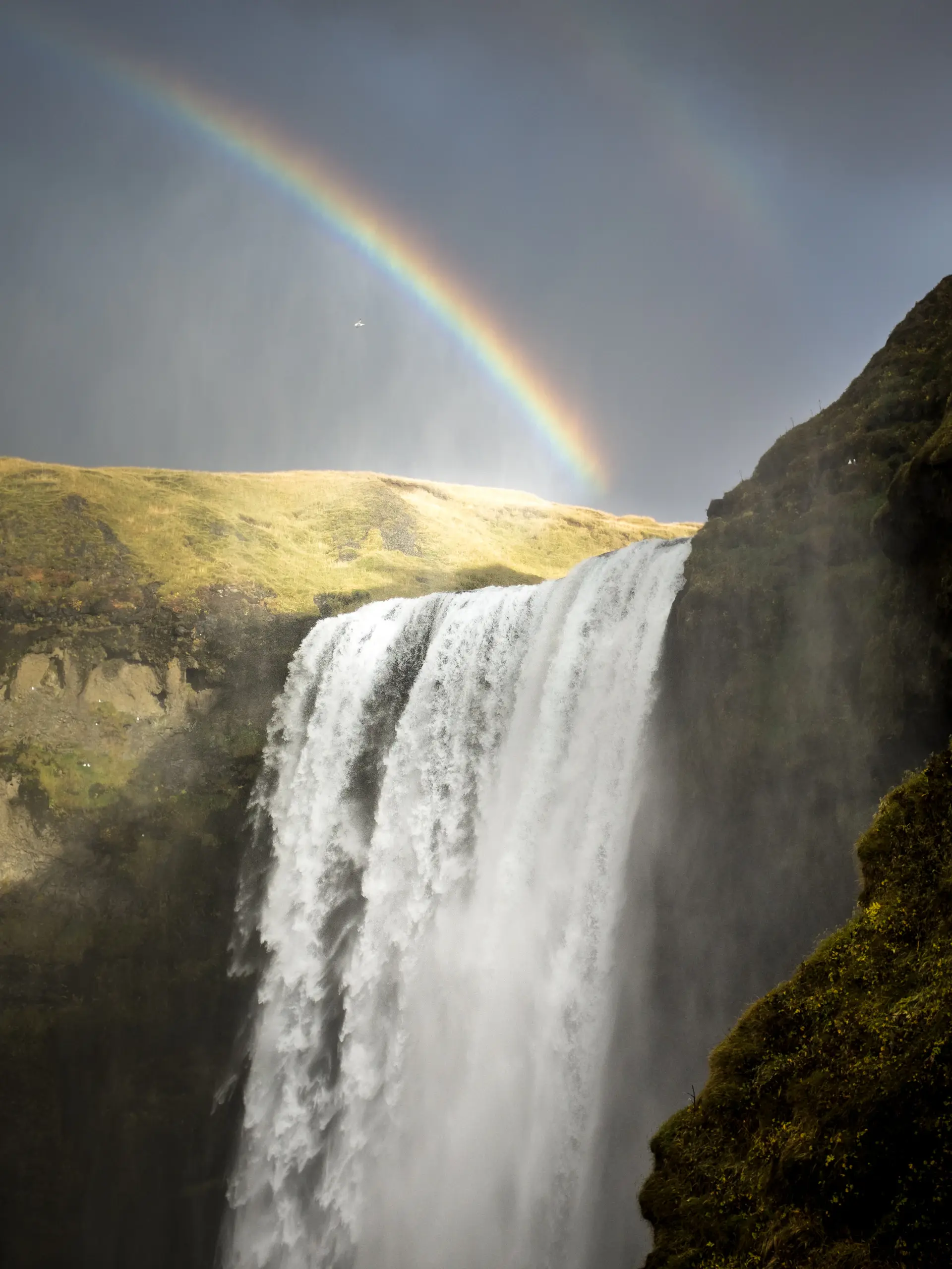 A rainbow forming in the spray of a sunlit waterfall