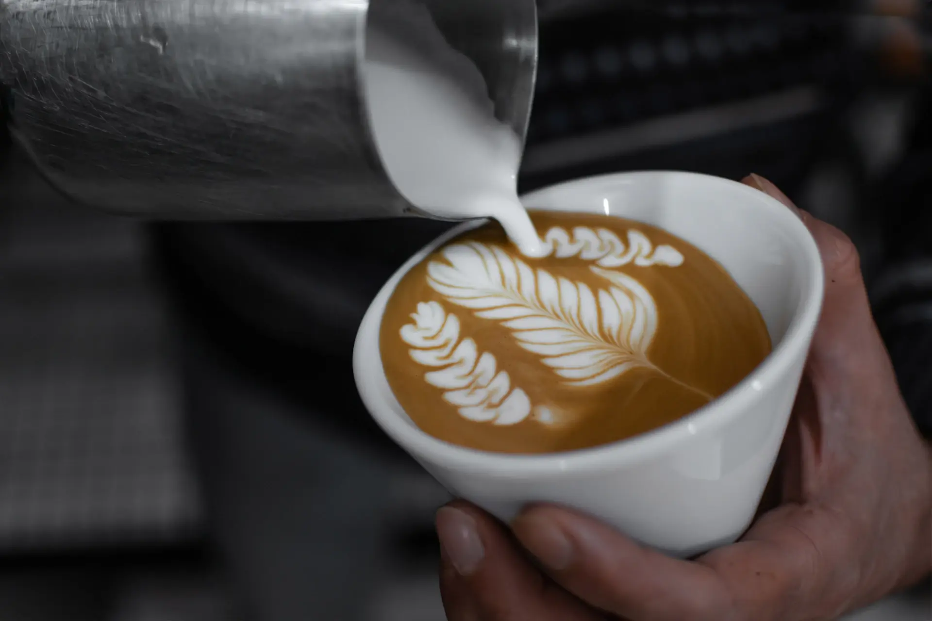 Barista pouring latte art on a warm-toned ceramic cup