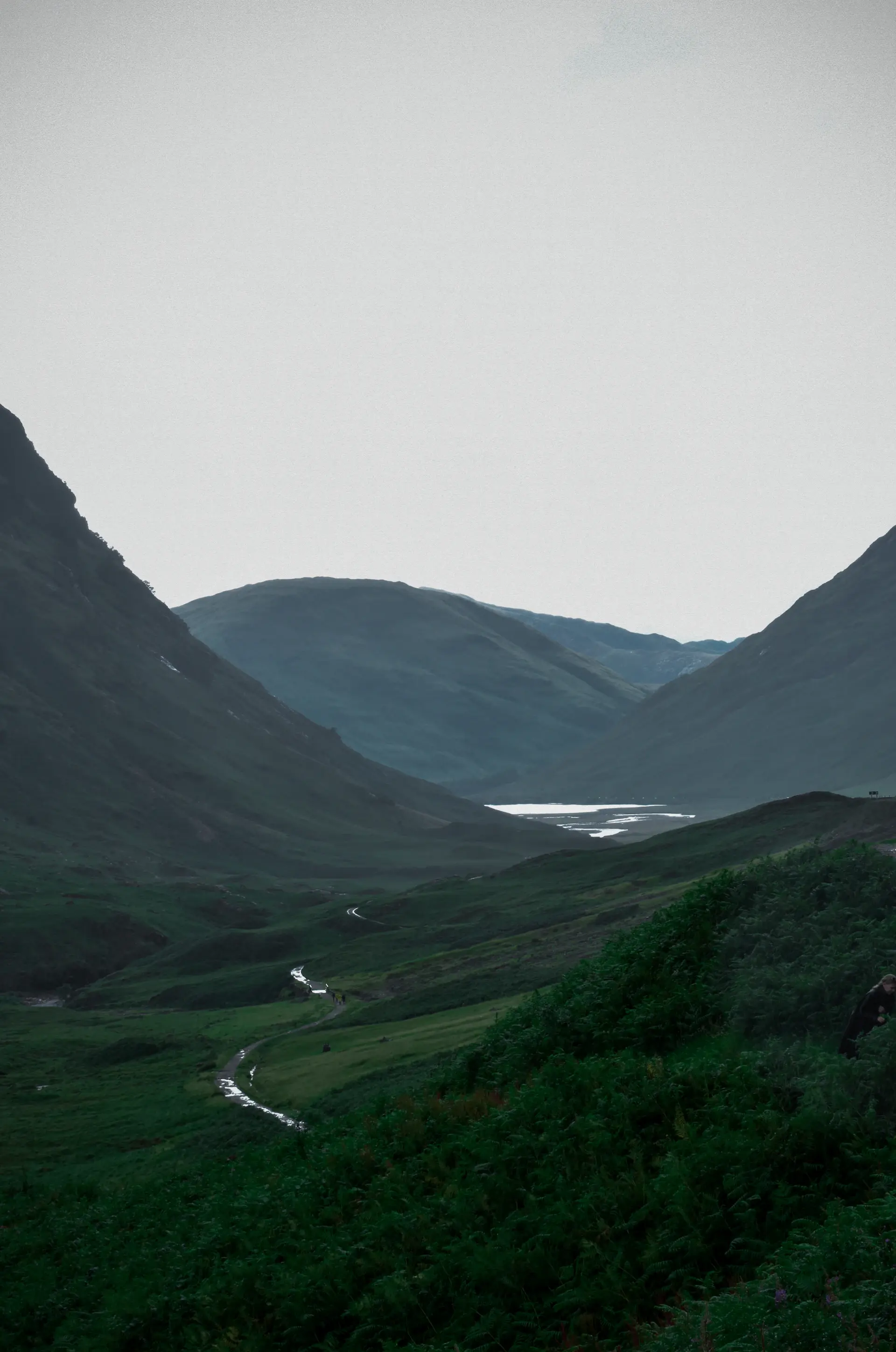 An empty green valley folding into distant hazy hills
