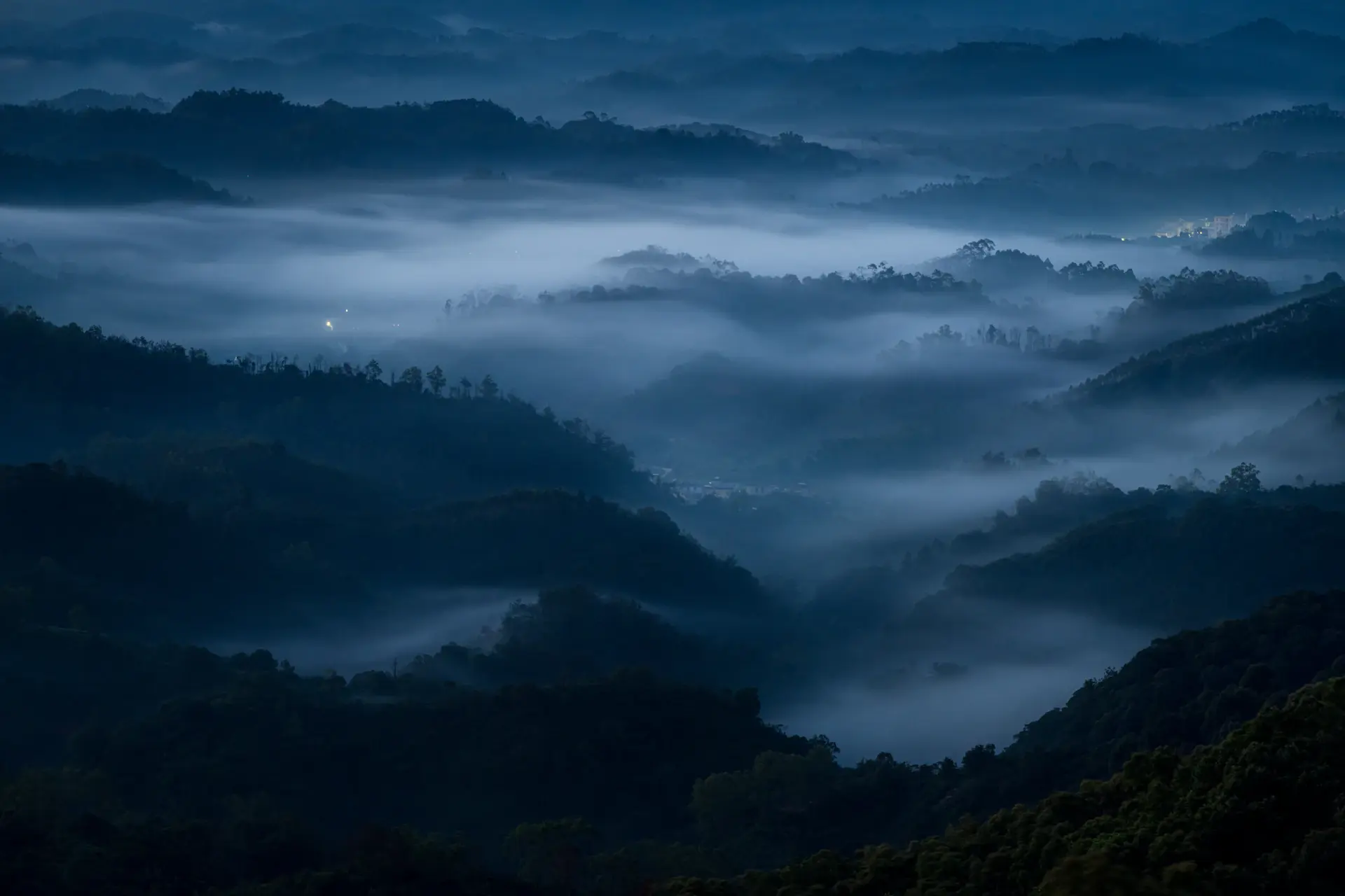 Dark misty mountain valley at blue hour with a single lit horizon