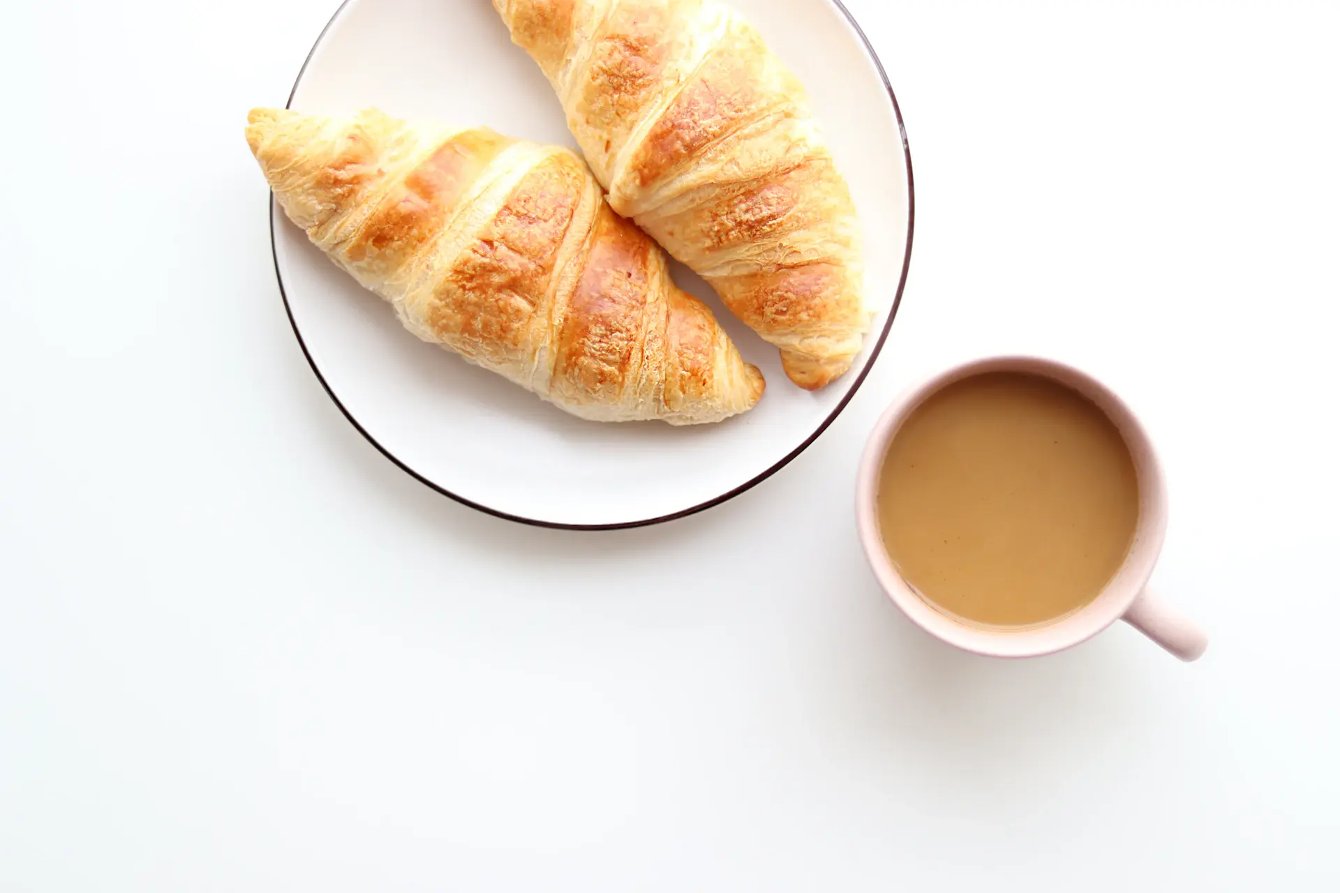 Coffee cup beside a croissant, illustrated in line art