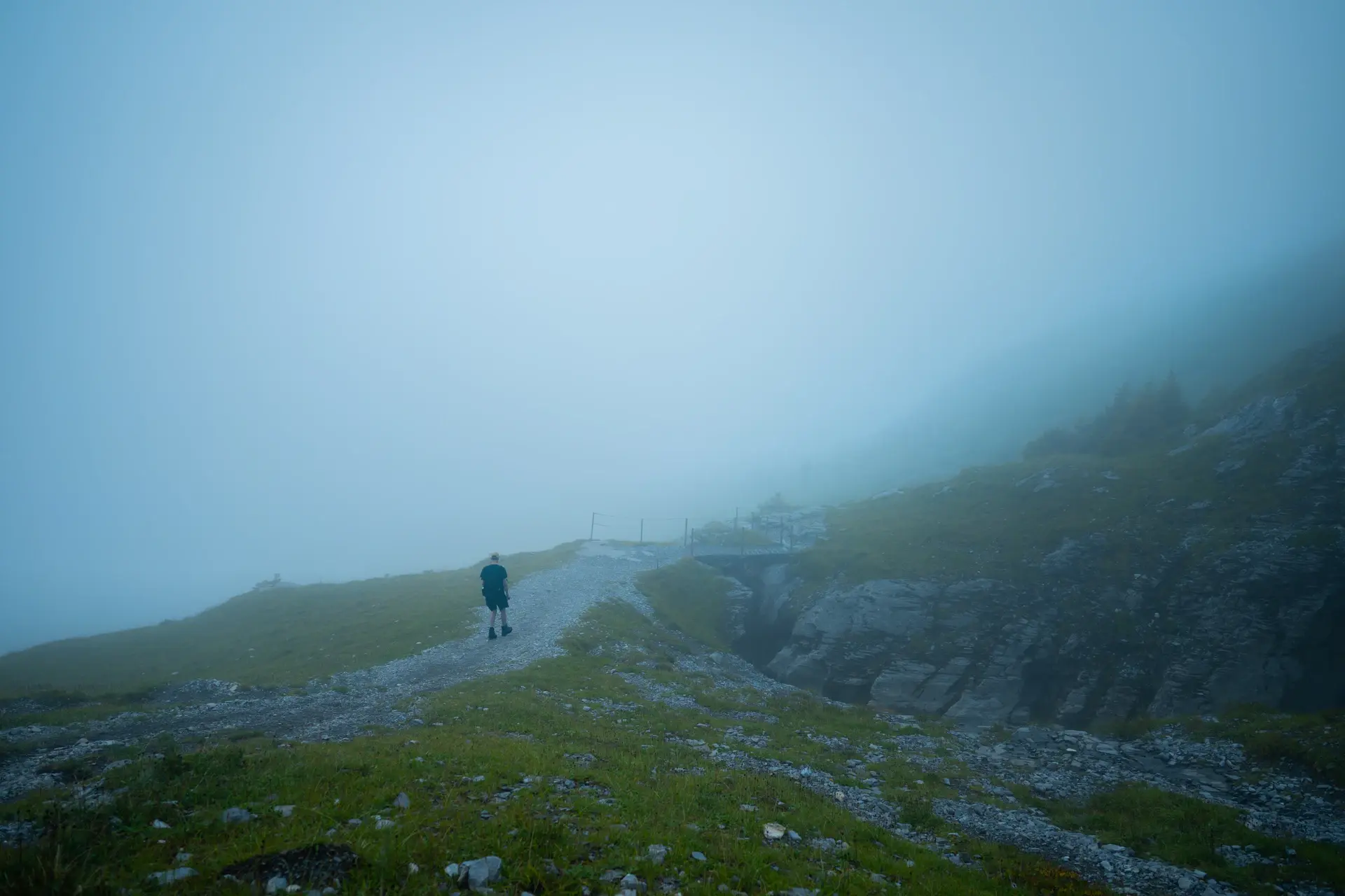 A traveller pausing on a misted mountain path at dawn