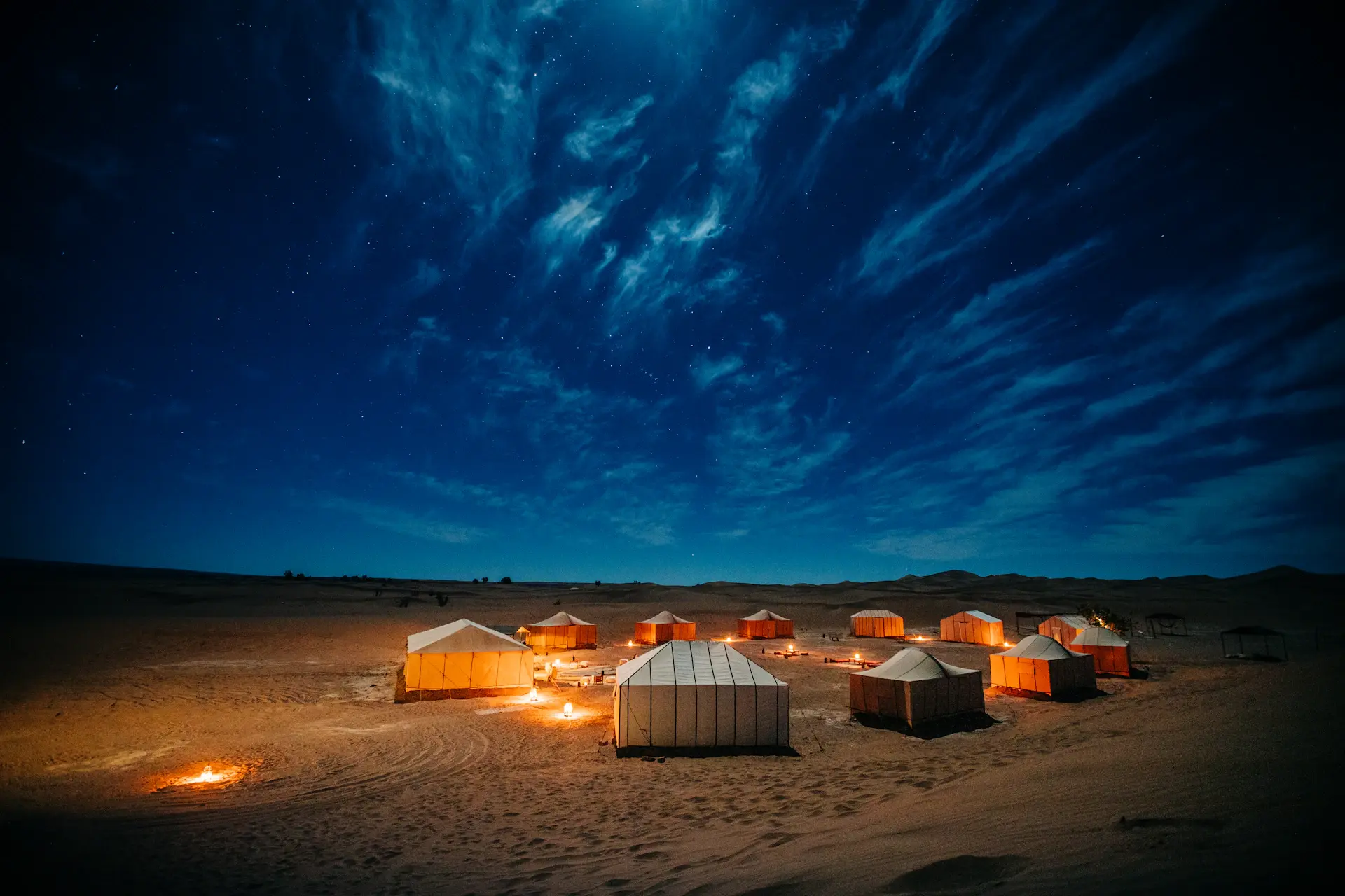 A solitary tent beneath desert dunes under stars