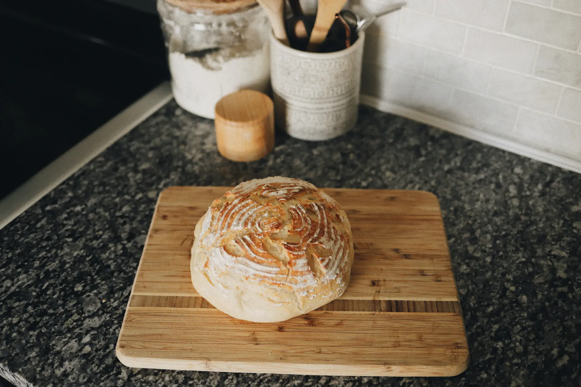 A scored sourdough loaf cooling on a wooden board