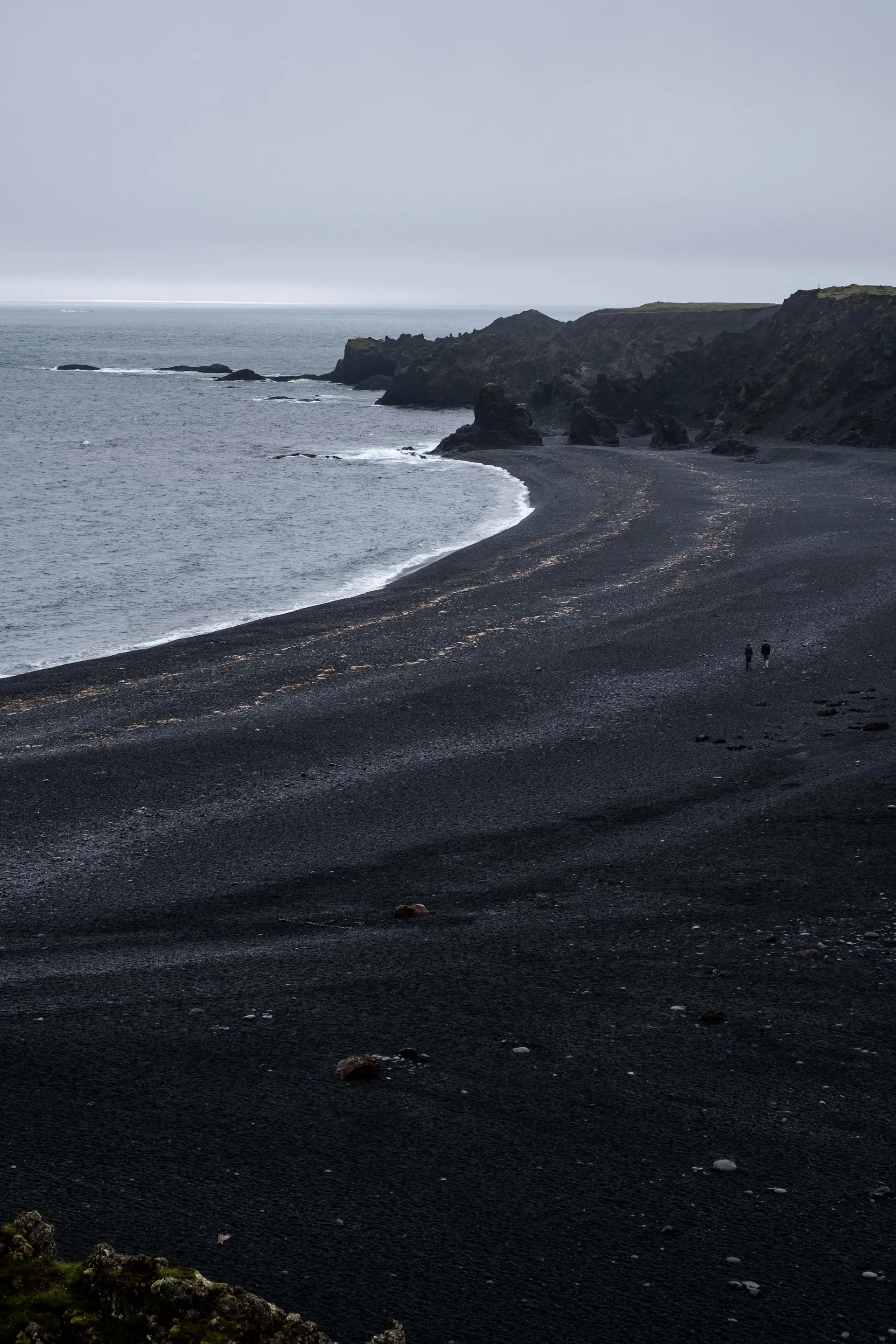 Foam tracing patterns across a black volcanic beach