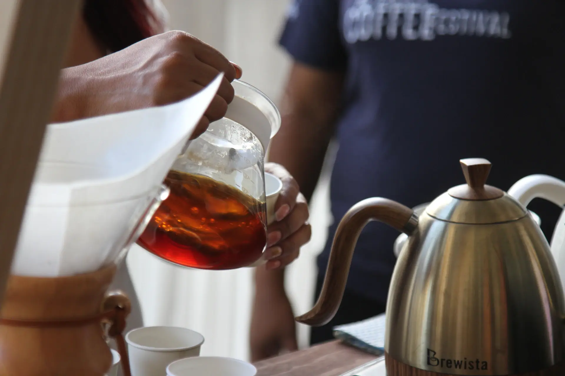 Hand pouring slow-brew coffee from an enamel kettle, soft afternoon light