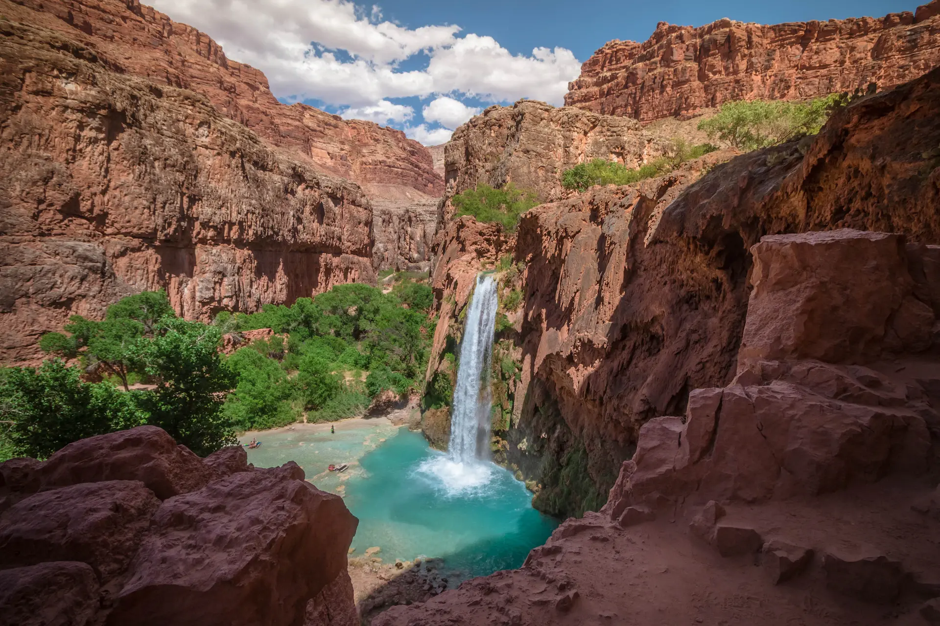 An immense cascade falling into a turquoise canyon pool