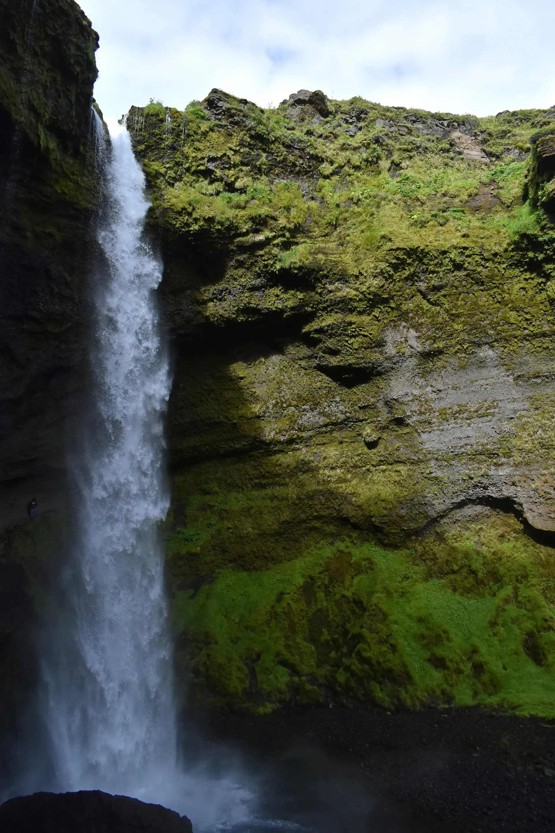 A thin waterfall falling down a sheer mossy wall