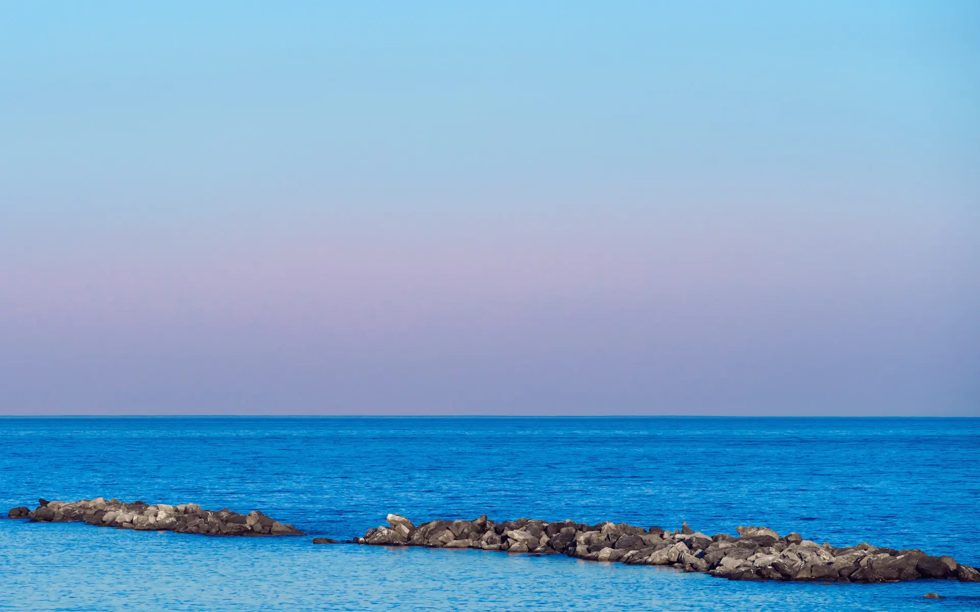 Still mirror-calm sea meeting low cliffs at blue hour