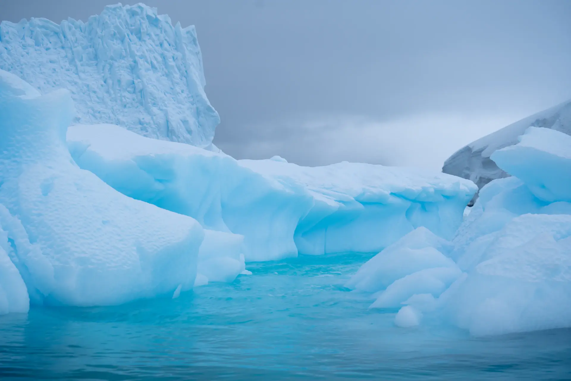 A solitary figure standing before a vast blue glacier at first light in Antarctica