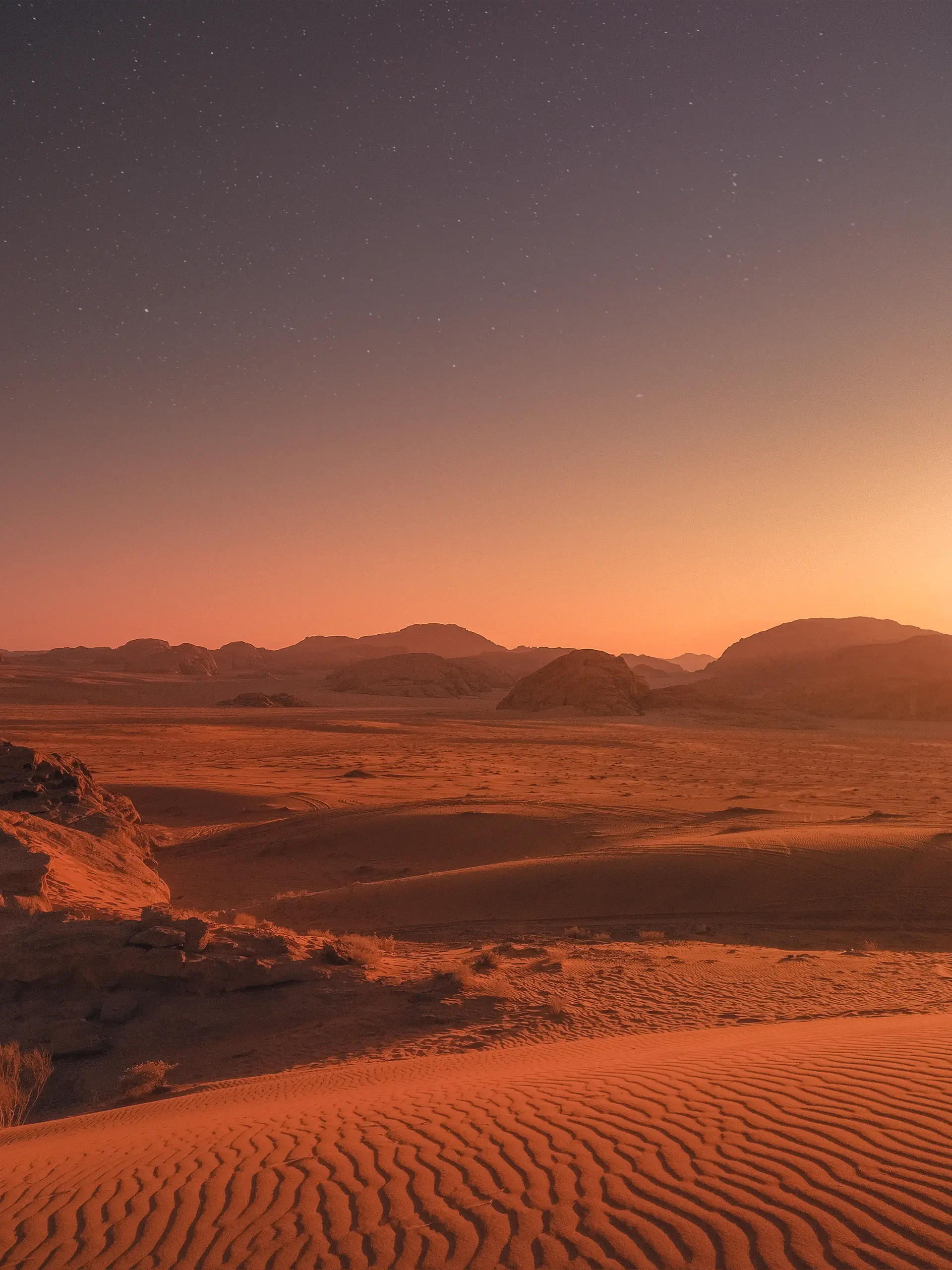 A solitary luxury camp beneath vast desert dunes at dusk